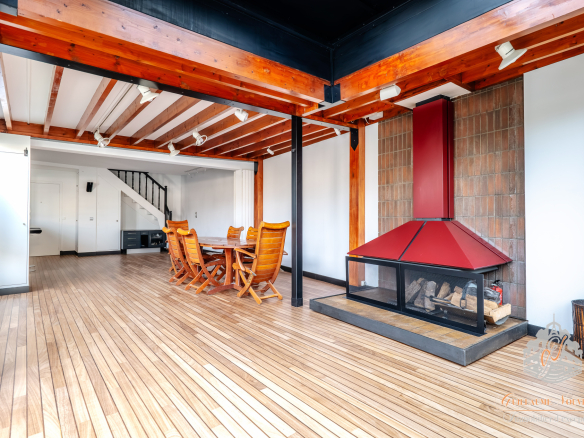 Intérieur d'un duplex avec poutres apparentes et cheminée, salle à manger en bois.