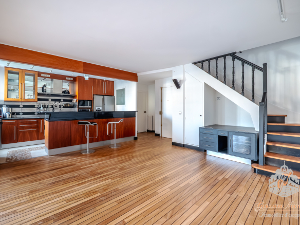Intérieur d'un duplex avec cuisine moderne, salon et escalier en bois, parquet au sol.