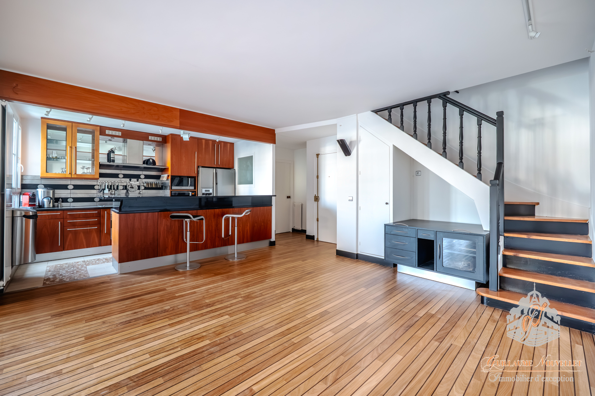 Duplex d’exception à Paris Intérieur d'un duplex avec cuisine moderne, salon et escalier en bois, parquet au sol.