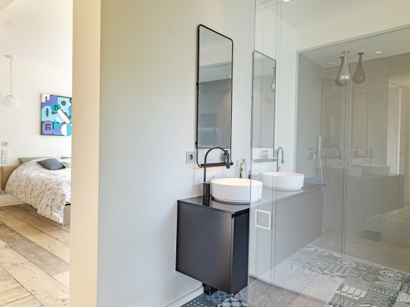 Modern bathroom with double vanity and glass shower, overlooking the bedroom