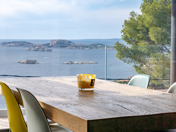 Panoramic sea view from a modern house with a wooden table and colorful chairs.