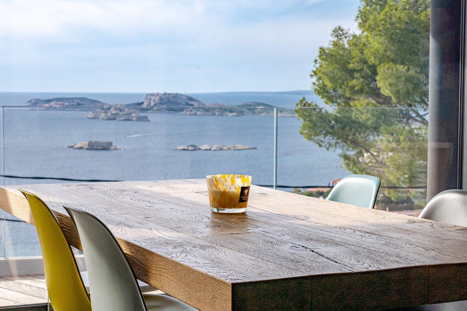 Contemporary house with sea view in Marseille Panoramic sea view from a modern house with a wooden table and colorful chairs.