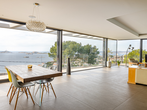 Modern interior of a villa with sea view, dining table and large bay windows.