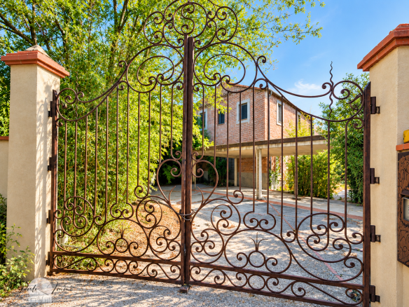 Wrought iron gate leading to an old property in Perpignan, surrounded by greenery.