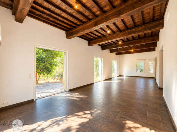 Interior of a renovated former wine cellar with wooden beams and tiled floor, bright and spacious.