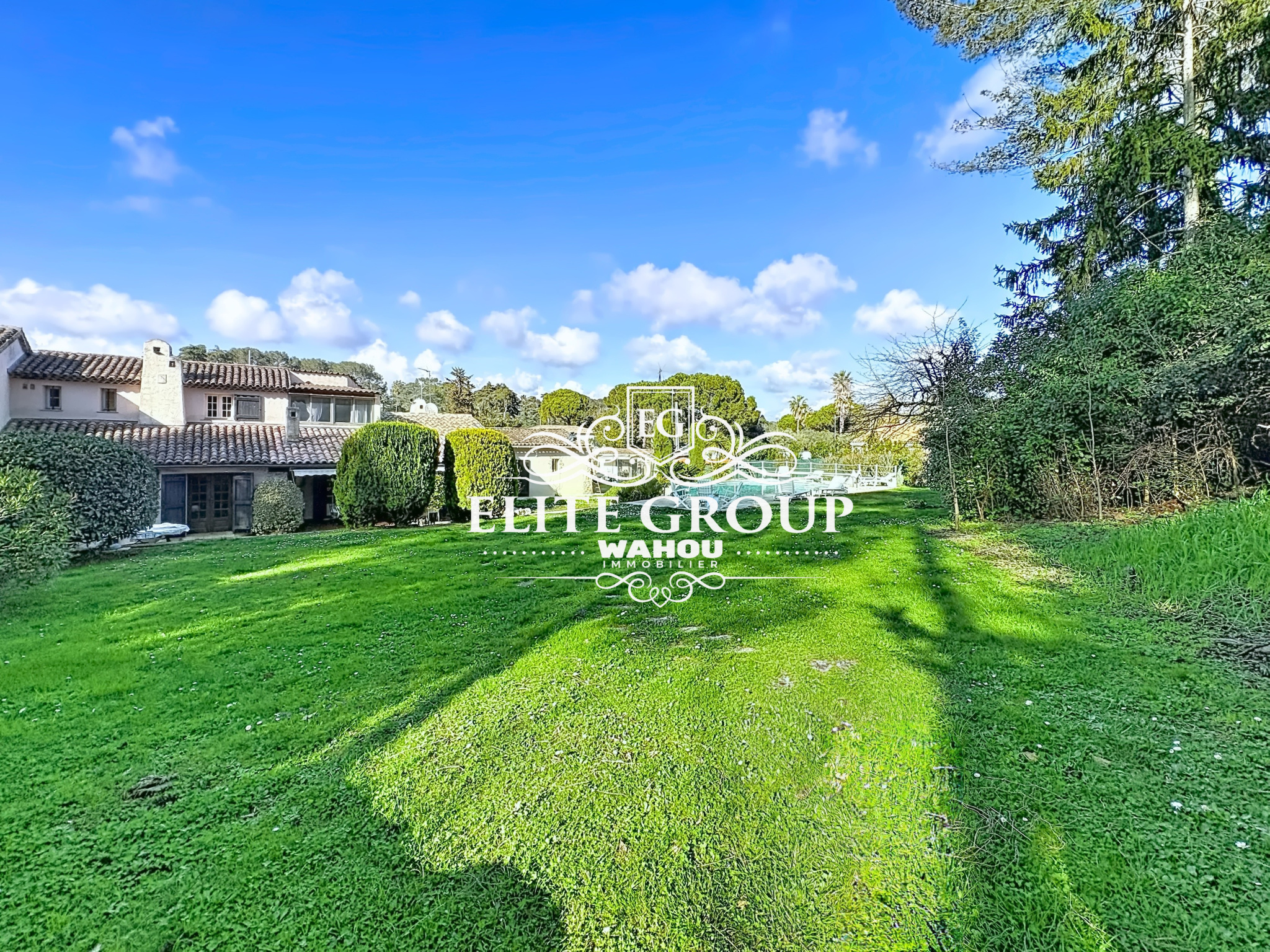 View of a green garden with a Provençal villa in Mougins, under a blue sky.