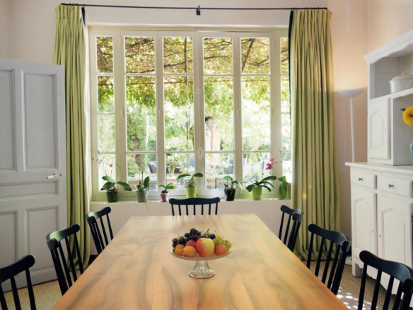 Dining room with a large wooden table and windows overlooking a garden.
