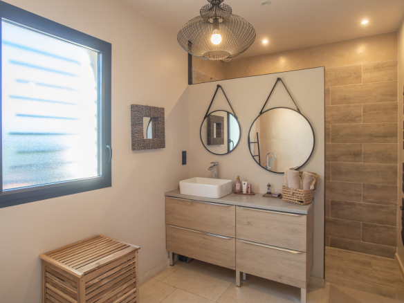Modern bathroom with wooden furniture and round mirror, natural light through the window.