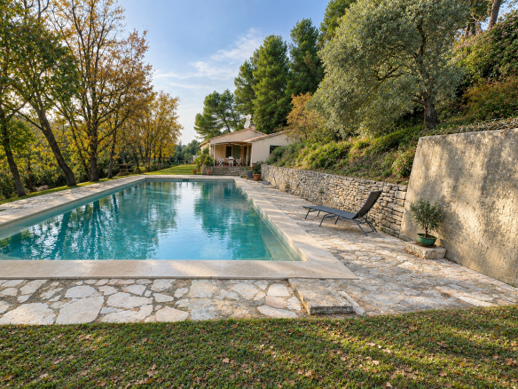 Single-storey house with swimming pool in Ménerbes, surrounded by trees and greenery.
