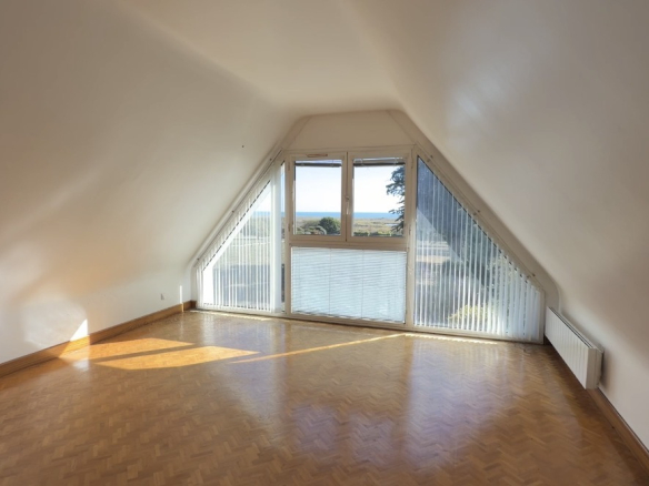 Intérieur d'une chambre avec vue sur la mer, grandes fenêtres et parquet en bois.