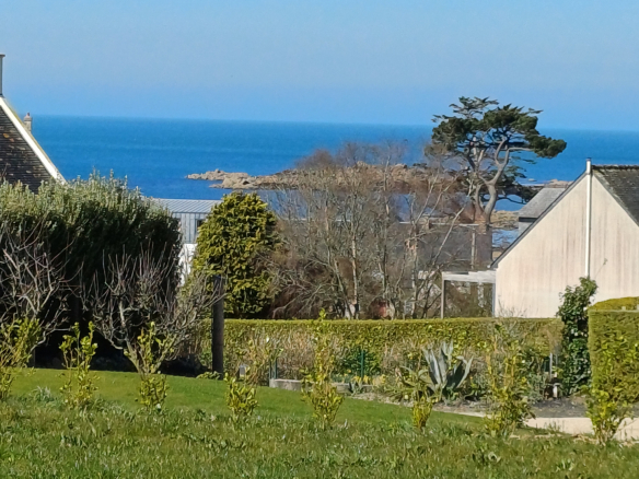 Vue sur la mer depuis une maison bretonne en pierre à Plougasnou, avec un jardin en premier plan.