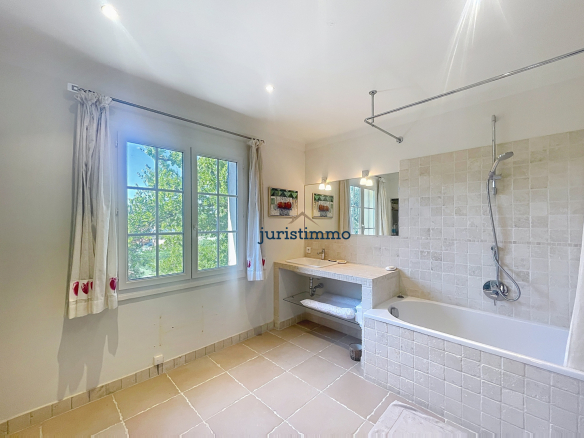 Salle de bain lumineuse avec baignoire et fenêtre donnant sur un jardin.