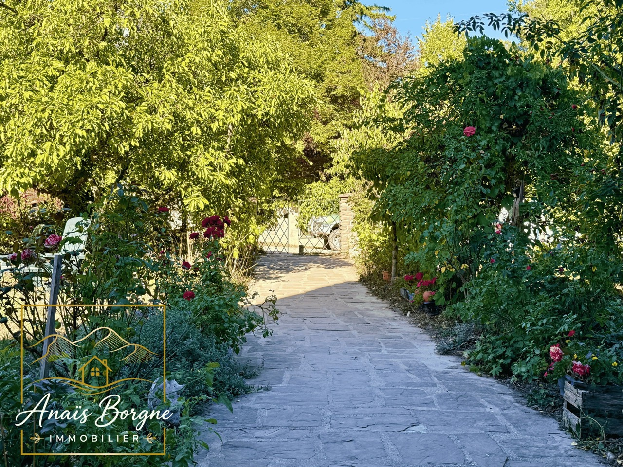Chemin vers un manoir Chemin menant à un manoir dans un parc arboré avec des fleurs et des arbres.