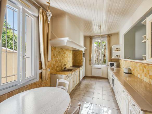 Cuisine lumineuse avec carrelage beige et fenêtres, dans une maison de caractère à Saint-Raphaël.