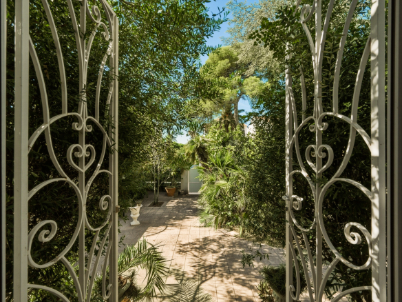 Vue d'un jardin clos avec des plantes et des arbres, encadrée par une porte en ferronnerie.