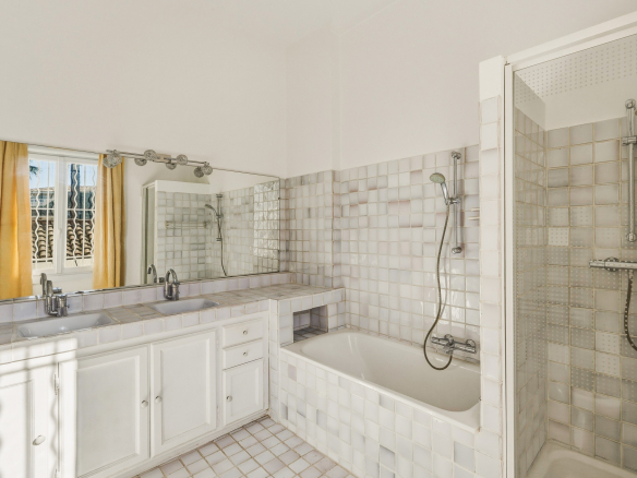 Salle de bain spacieuse avec baignoire et douche, carrelage clair et miroir.