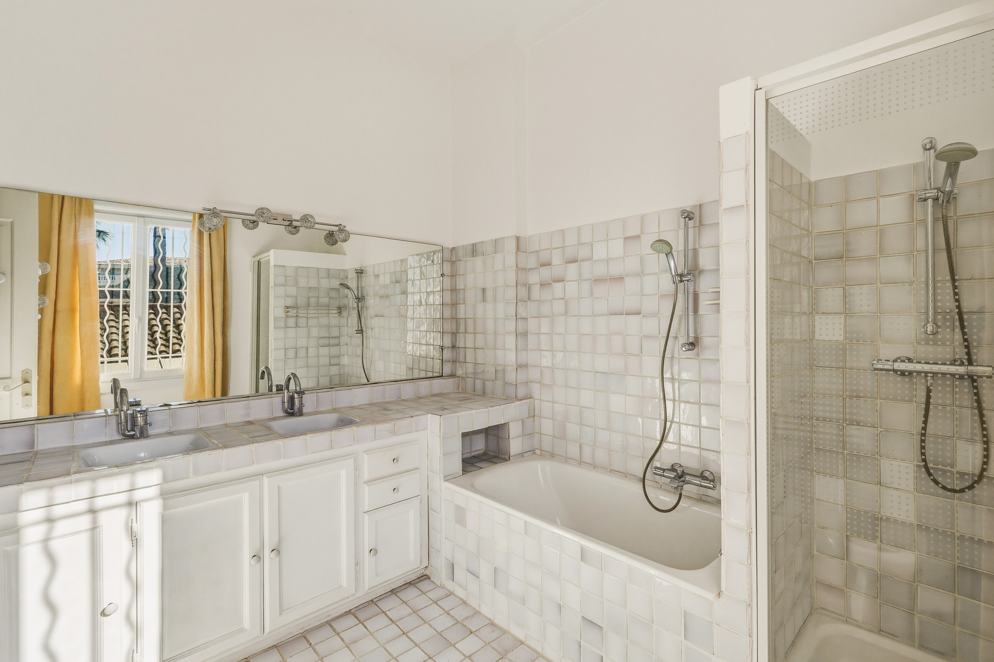 Salle de bain de maison à Saint-Raphaël Salle de bain spacieuse avec baignoire et douche, carrelage clair et miroir.