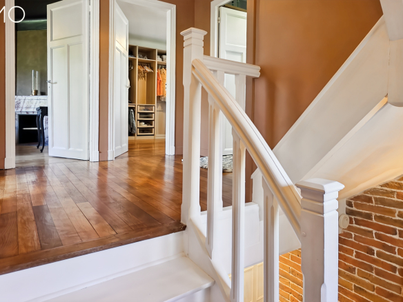 Escalier central en bois peint dans une maison meulière à Arpajon, avec murs en briques et couleurs chaleureuses.