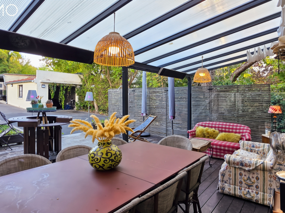 Terrasse couverte avec mobilier en bois et en rotin, décorée de plantes et luminaires, à Arpajon.