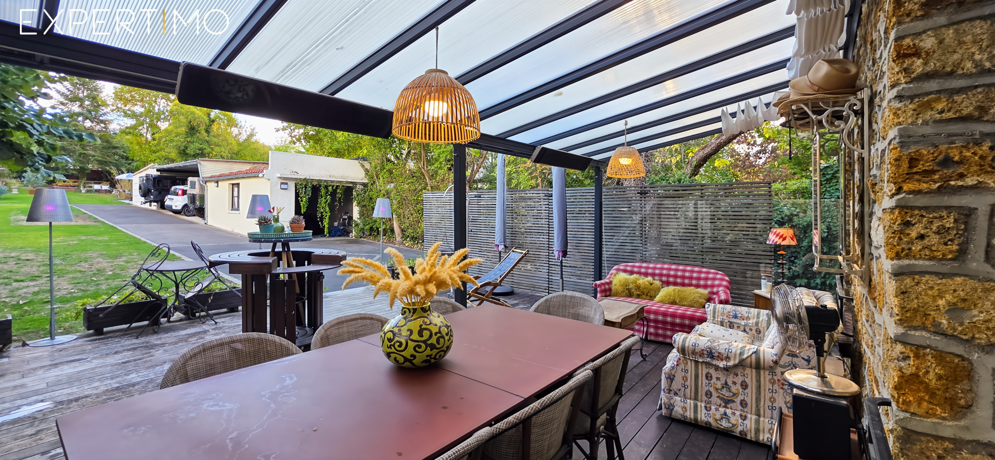 Terrasse d’une meulière à Arpajon Terrasse couverte avec mobilier en bois et en rotin, décorée de plantes et luminaires, à Arpajon.
