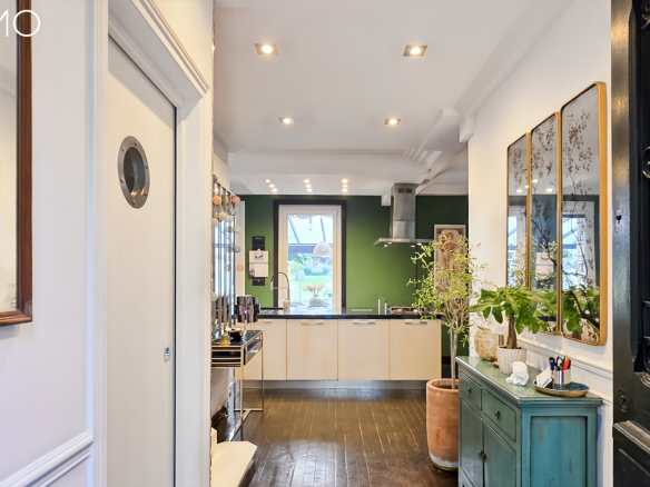 Intérieur d'une meulière à Arpajon avec un couloir menant à la cuisine, décoré de plantes et de tableaux.