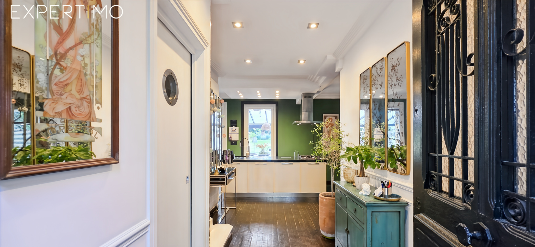 Intérieur d’une meulière à Arpajon Intérieur d'une meulière à Arpajon avec un couloir menant à la cuisine, décoré de plantes et de tableaux.