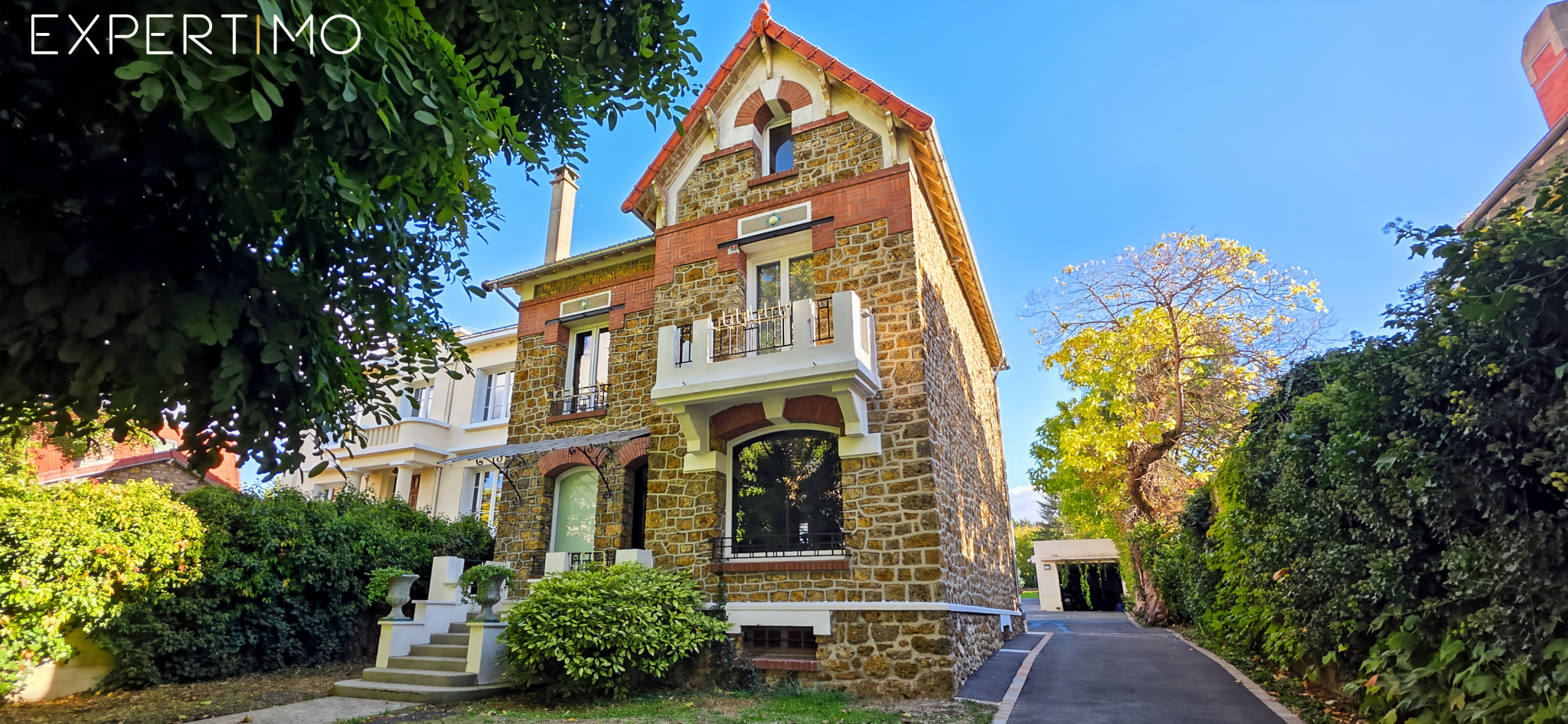 Meulière à Arpajon Maison meulière en pierre et brique à Arpajon, avec jardin paysager et escalier central en bois.