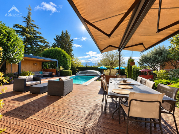 Terrasse en bois avec mobilier de jardin et piscine, vue sur la nature et le ciel bleu.