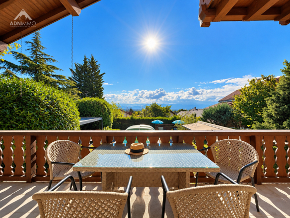 Terrasse d'un chalet avec vue sur le Mont-Blanc et Genève, ensoleillée, entourée de verdure.