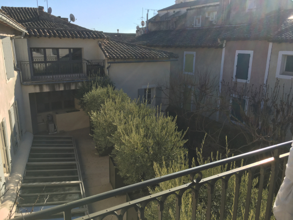 View of an interior garden with olive trees and historic buildings in L'Isle-sur-la-Sorgue.