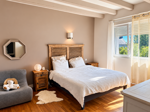 Chambre lumineuse avec lit double, meubles en bois et coin salon, dans une maison à Auray.