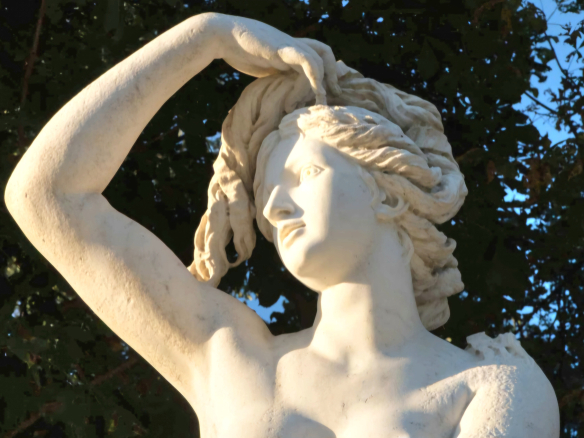 Statue en marbre représentant une femme avec les cheveux au vent, dans un parc.