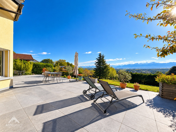 Terrasse de maison avec chaises longues et vue sur les montagnes sous un ciel bleu.