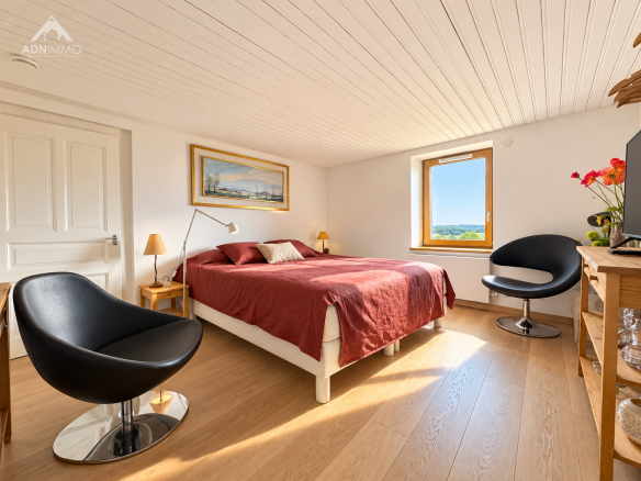 Chambre d'une maison rénovée avec lit double et fauteuils modernes, lumière naturelle.
