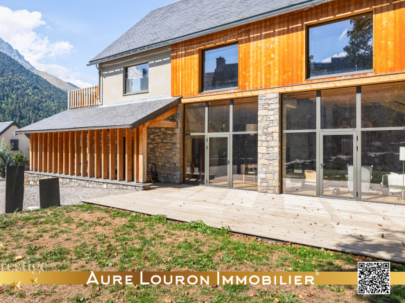 Chalet rénové avec terrasse en bois et grandes baies vitrées, entouré de montagnes.