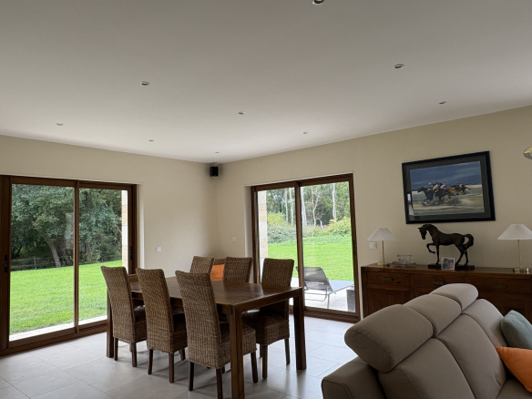 Intérieur d'une propriété avec une salle à manger et des fenêtres donnant sur un jardin verdoyant.