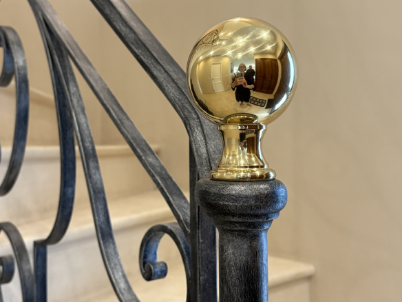 Garde-corps en métal avec une boule dorée au sommet, escalier en marbre en arrière-plan.