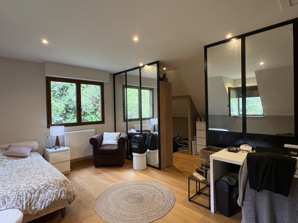 Chambre d'une propriété avec un lit, un fauteuil et des fenêtres donnant sur la verdure.