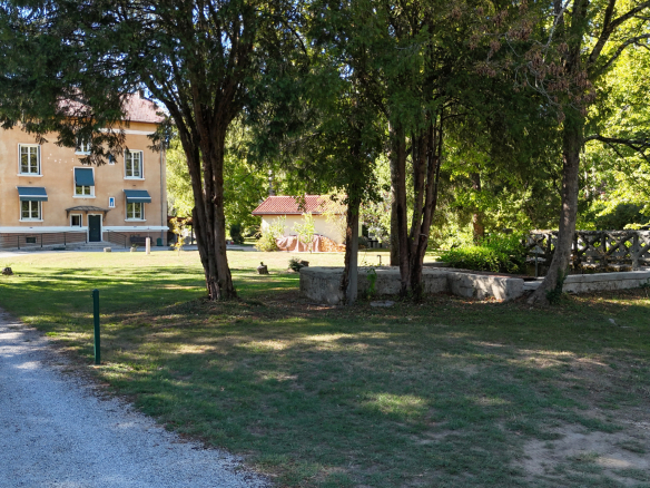 Property on the banks of the Ain river, surrounded by trees in a wooded park.