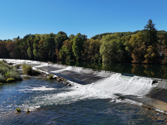 View of the Ain river with waterfalls and trees in the background.