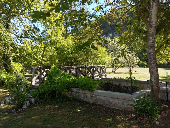 View of a wooded park with a stone wall and trees on the banks of the Ain river.