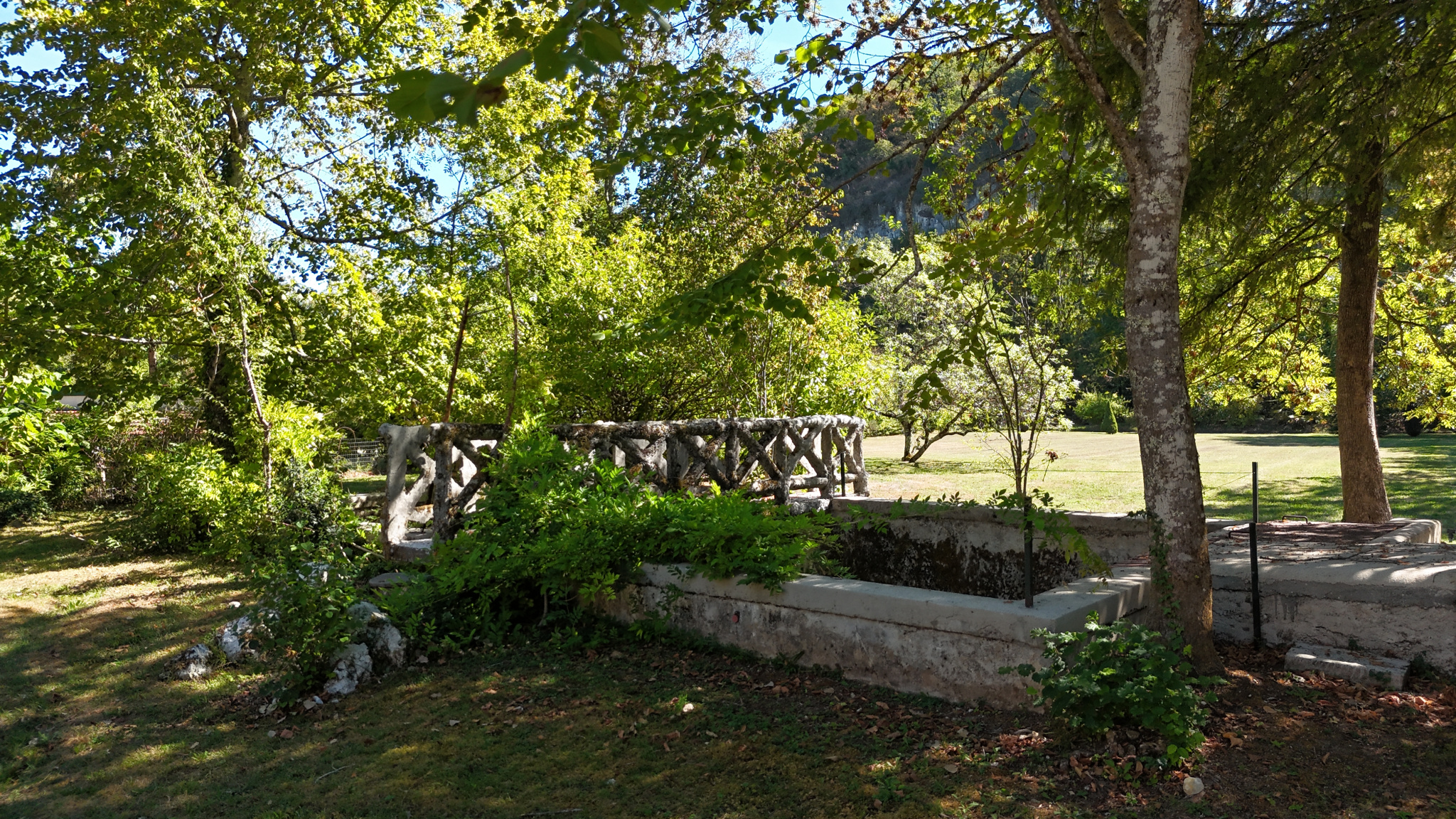 Property on the banks of the Ain river View of a wooded park with a stone wall and trees on the banks of the Ain river.