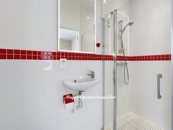 Salle de bain moderne avec douche et lavabo, carrelage blanc et rouge.
