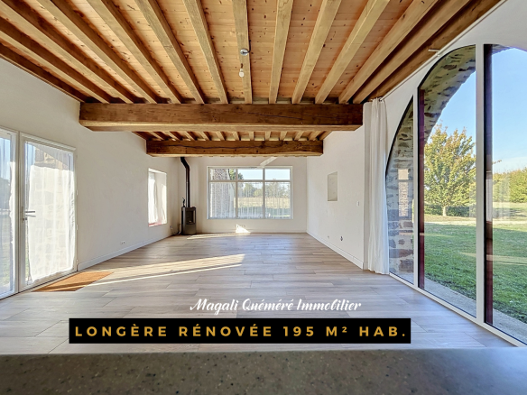 Intérieur d'une longère rénovée de 195 m² avec poutres apparentes et grandes fenêtres.