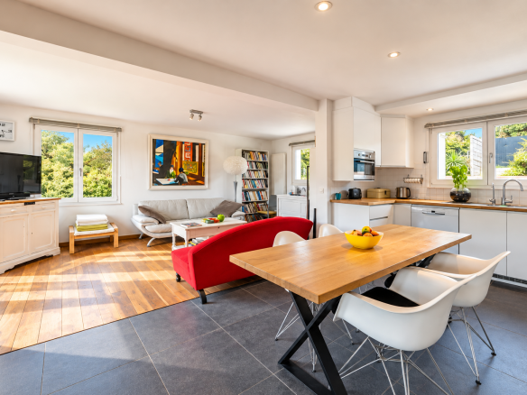 Intérieur d'une villa moderne avec cuisine ouverte, salon lumineux et vue sur la nature.