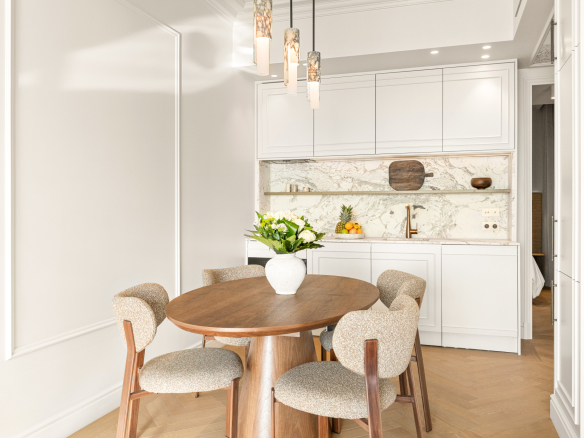 Interior of a renovated apartment with a round table and chairs, overlooking a modern kitchen.