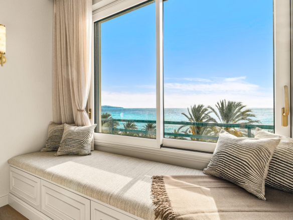 Fenêtre d'un appartement avec vue panoramique sur la mer Méditerranée et des palmiers à Nice.