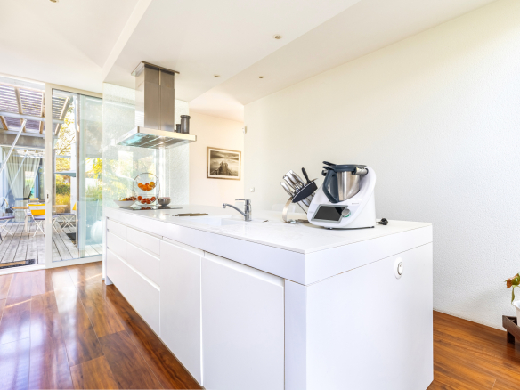 Cuisine moderne d'une maison d'architecte avec un plan de travail blanc et un accès à l'extérieur.