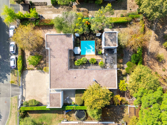 Vue aérienne d'une maison d'architecte de plain-pied avec piscine, jardin paysager et forêt environnante.