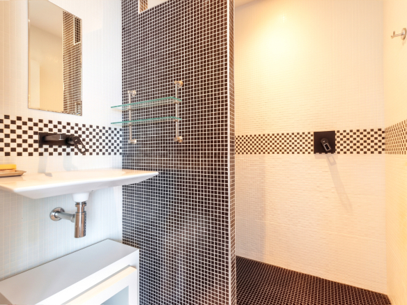 Salle de bain moderne avec douche et lavabo, carrelage noir et blanc.